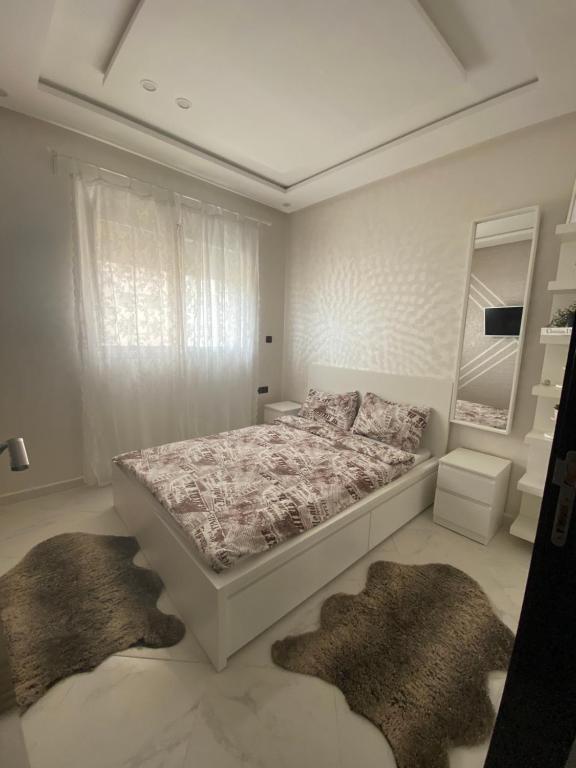 Appartement prestige في القنيطرة: غرفة نوم بيضاء بسرير وسجادتين