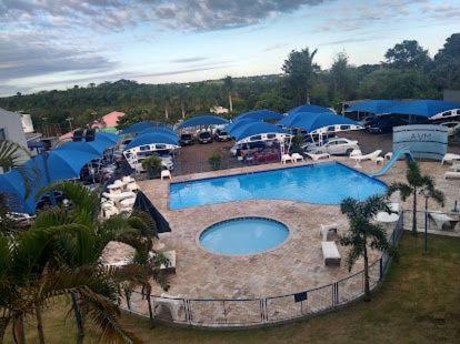 a large swimming pool in a parking lot with blue umbrellas at Hotel AVM in Foz do Iguaçu