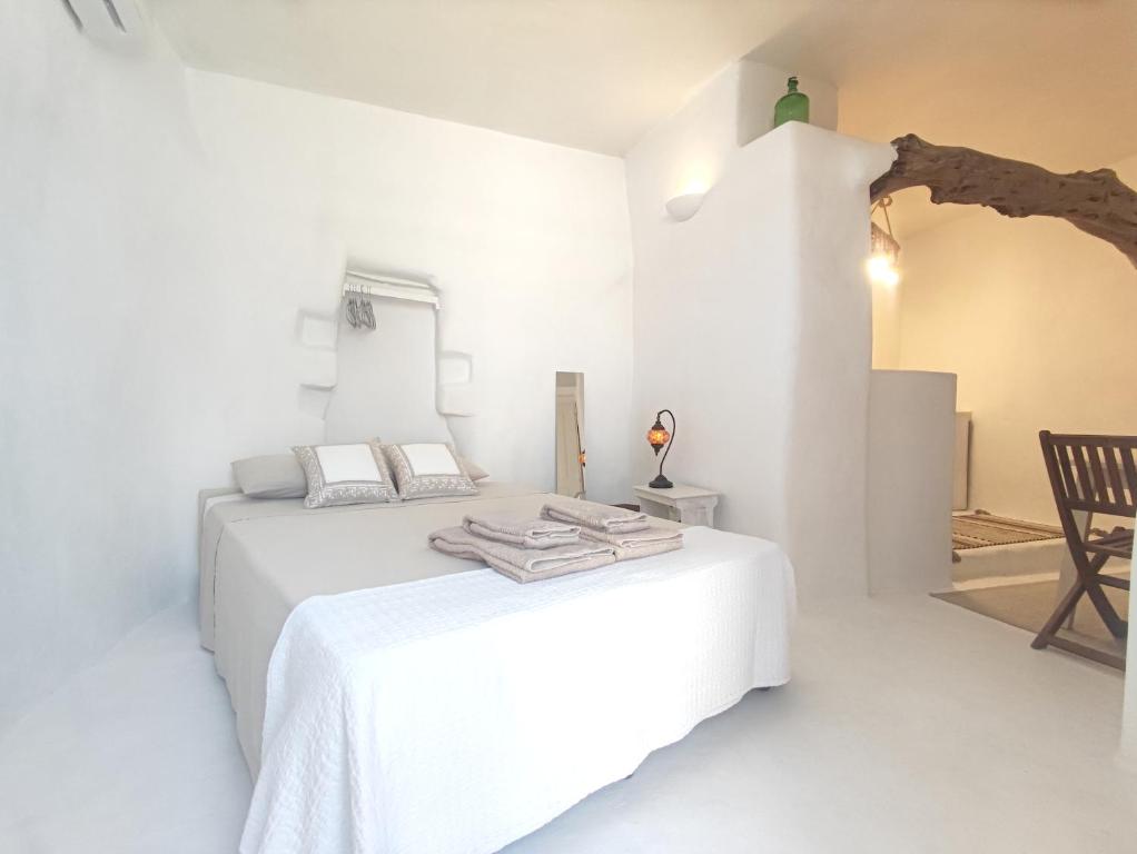 a white bedroom with two beds and a chair at Καμάρα (Kamara) cave rooms in Triovasálos
