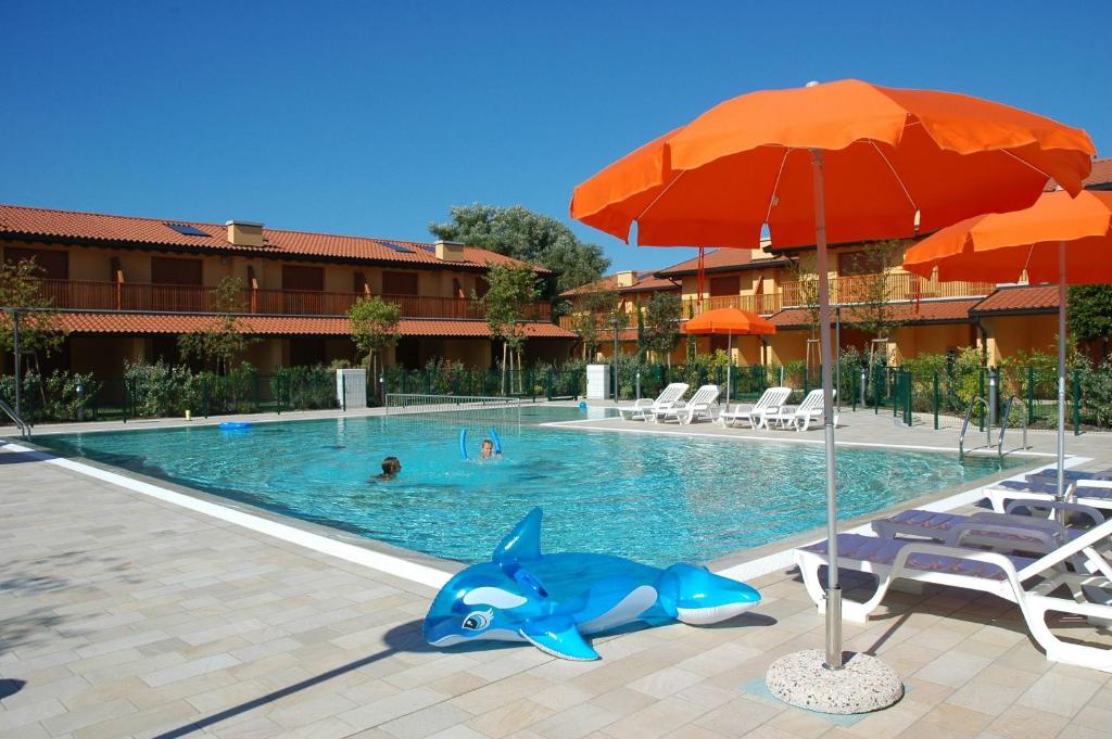 einen Pool mit einem blauen Delfin und einem Sonnenschirm in der Unterkunft Villaggio Tamerici in Lignano Sabbiadoro