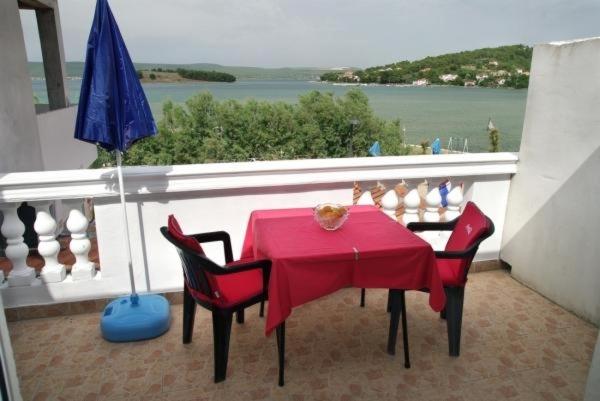 a red table with chairs and an umbrella on a balcony at Apartmentsin Pasman with Air condition, WIFI 4650-1 -2 in Pašman