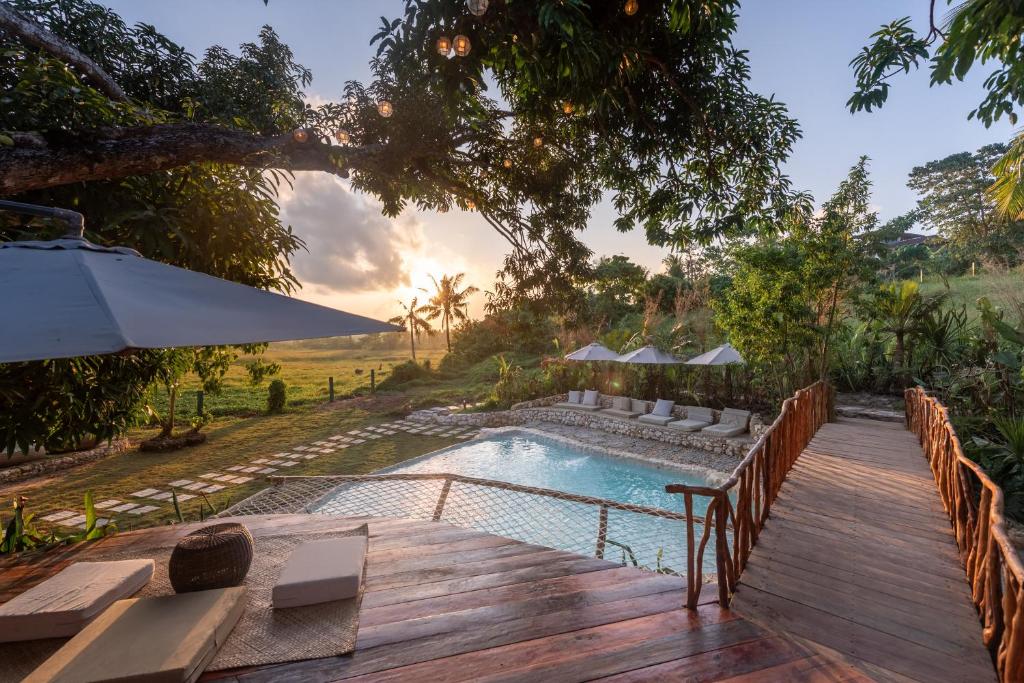 une terrasse en bois à côté d'une piscine avec un parasol dans l'établissement The Hillside Resort Siargao, à General Luna