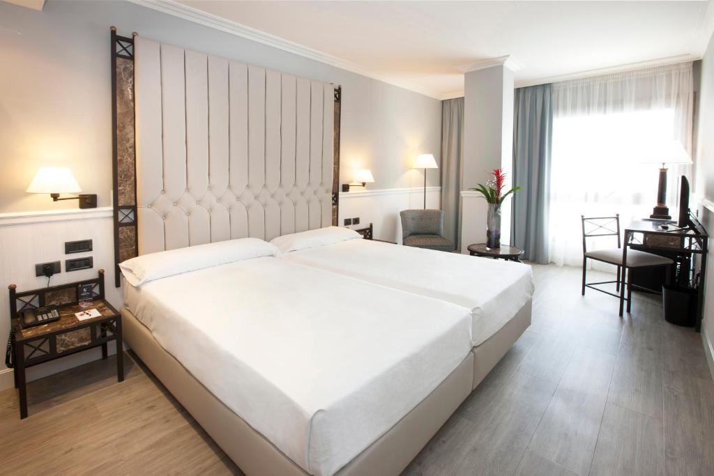 a bedroom with a large white bed and a desk at Hotel Gran Via in Logroño