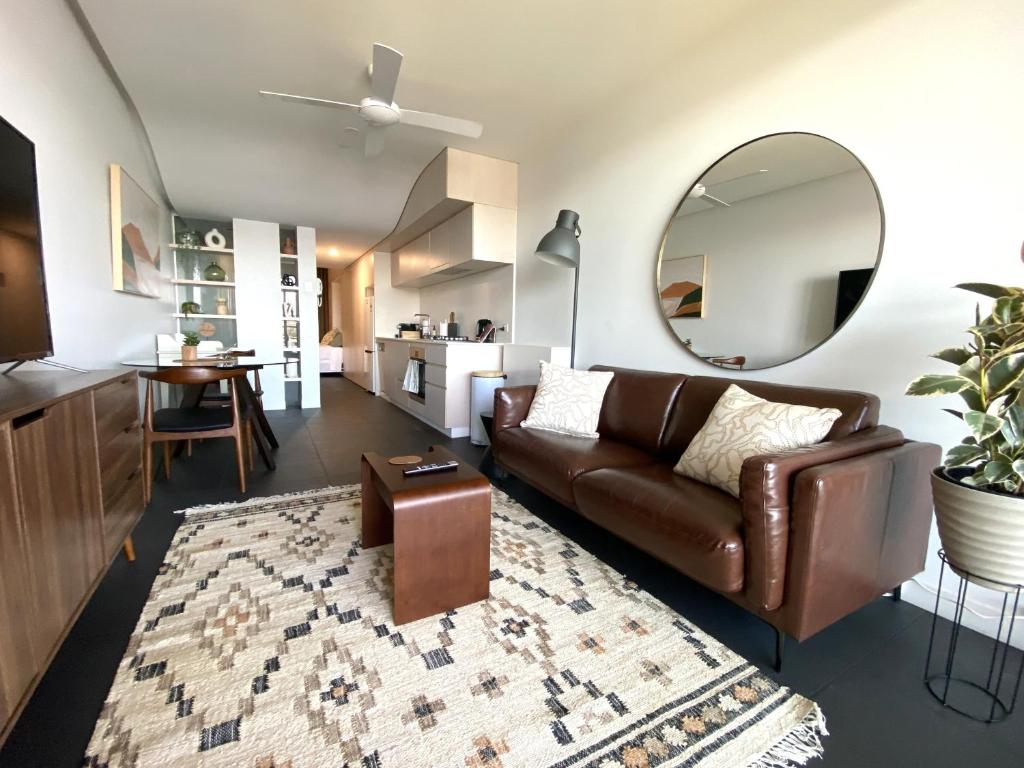 a living room with a brown leather couch and a mirror at Stylish Central Lake View Apartment in Canberra