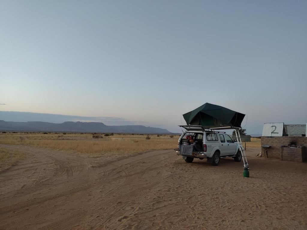een wit voertuig geparkeerd op een onverharde weg in de woestijn bij Canyon Farmyard Camping in Keetmanshoop