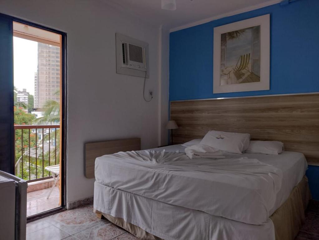 1 dormitorio con 1 cama con pared azul y ventana en Astúrias Praia Hotel en Guarujá