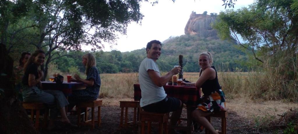 een groep mensen aan tafels met een berg op de achtergrond bij the walawwa guest house and hostel in Sigiriya