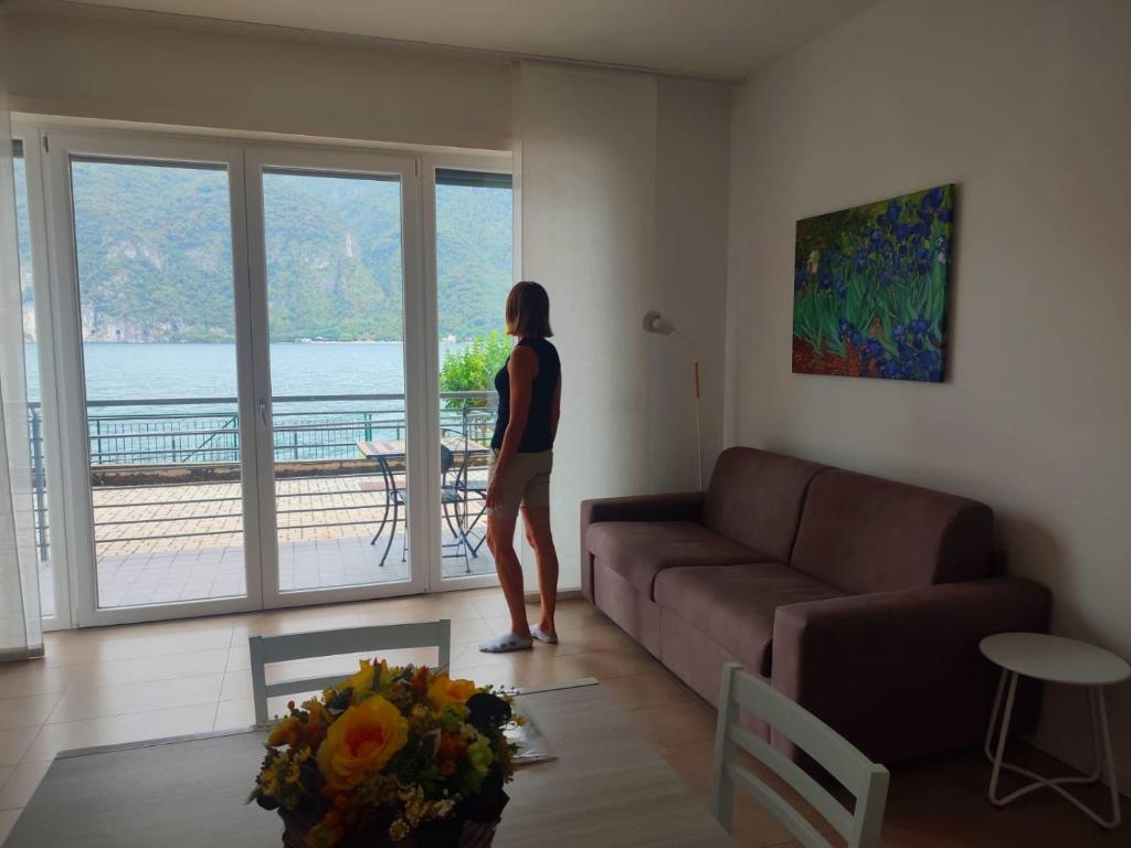 Una donna in piedi in un soggiorno che guarda fuori dalla finestra di Lake Como Casa la Rosa apartment Iris ad Abbadia Lariana