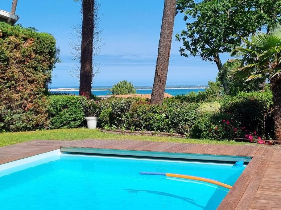 a blue swimming pool with the ocean in the background at Villa sur la dune, superbe vue, jacuzzi, piscine chauffée in La Teste-de-Buch