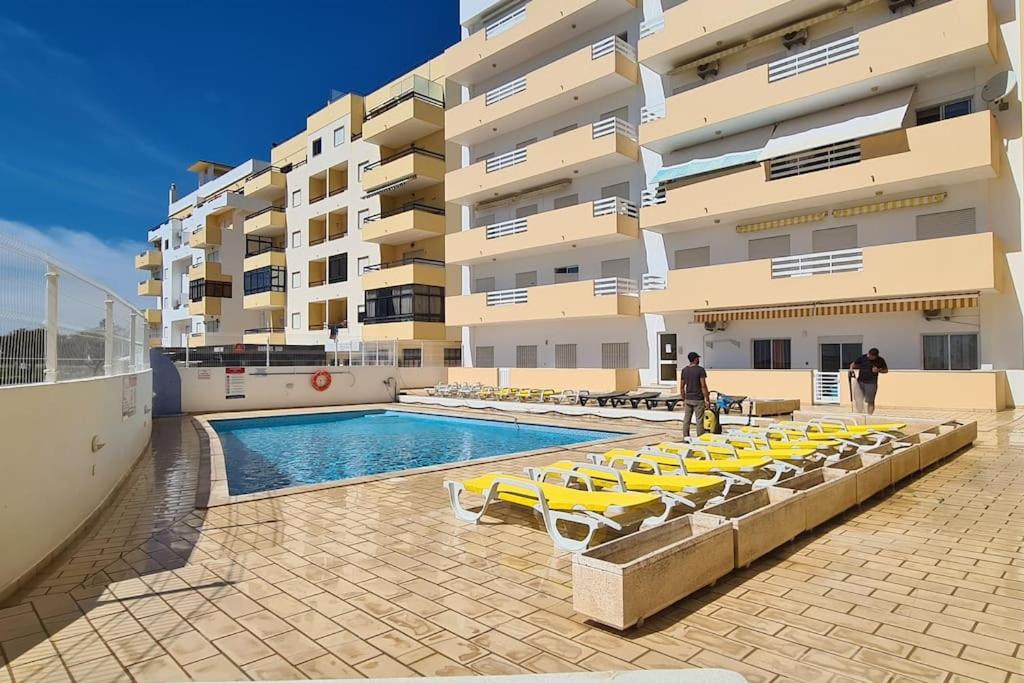 uma piscina com espreguiçadeiras amarelas ao lado de um edifício em Vilamoura-Quarteira Beaches Apt with pool and sea view em Quarteira