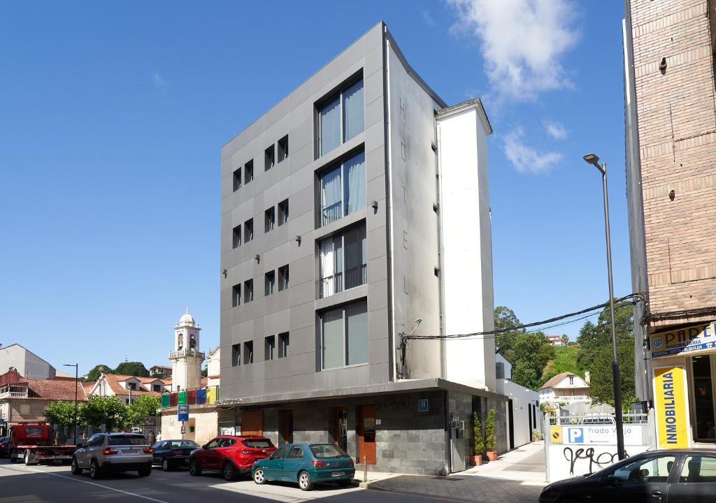 un edificio blanco alto en una calle de la ciudad con coches en Hotel Prado Viejo, en Moaña