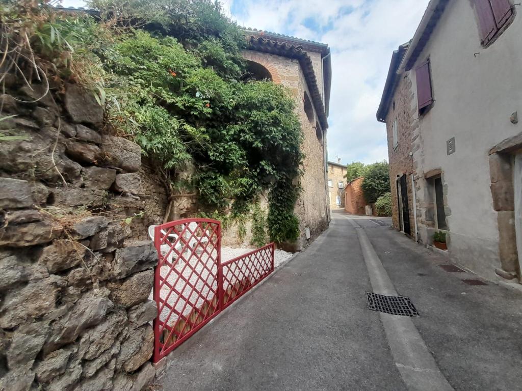 an alley with a red gate on the side of a stone wall at Gîte Olivia in Saint-Florent-sur-Auzonnet