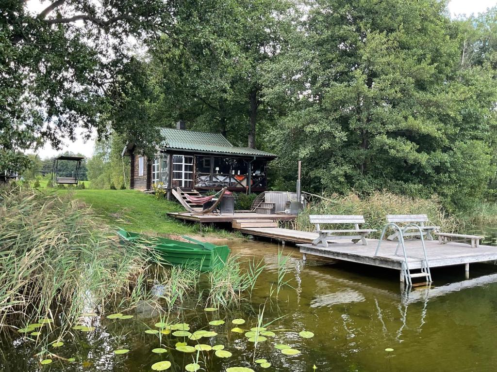 a cabin on a river with two benches on a dock at Poilsis prie Žeimenio ežero in Kaltanėnai