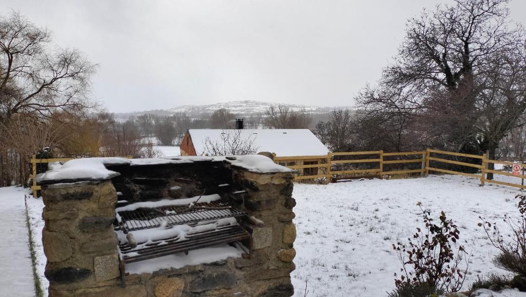 a stone fireplace in a snow covered yard with a fence at Maison en Cerdagne avec belle vue in Enveitg