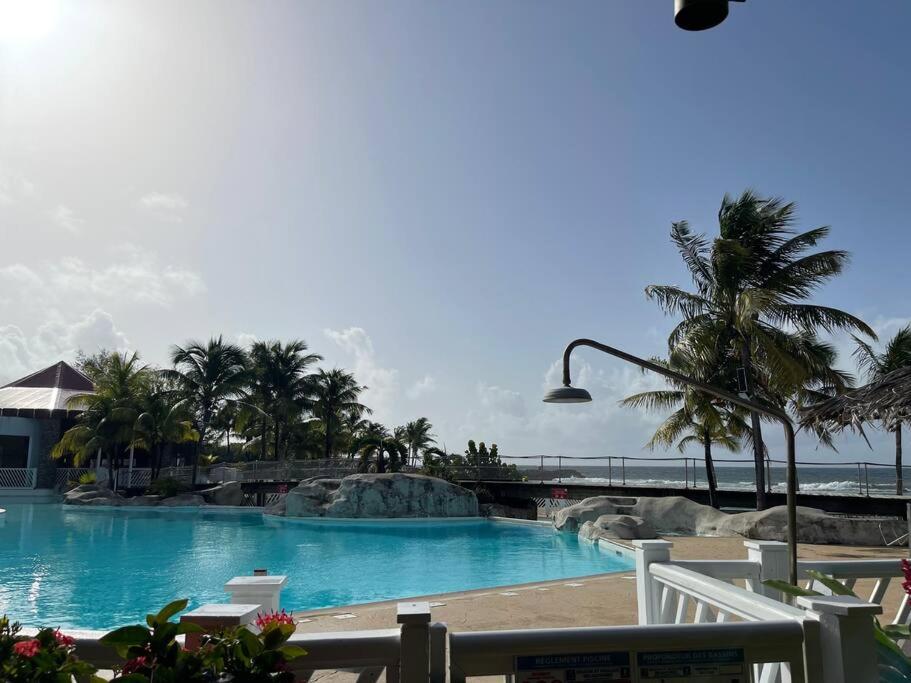 Una gran piscina con palmeras y el océano. en Appartement T2 climatisé La pépite, en Saint-François