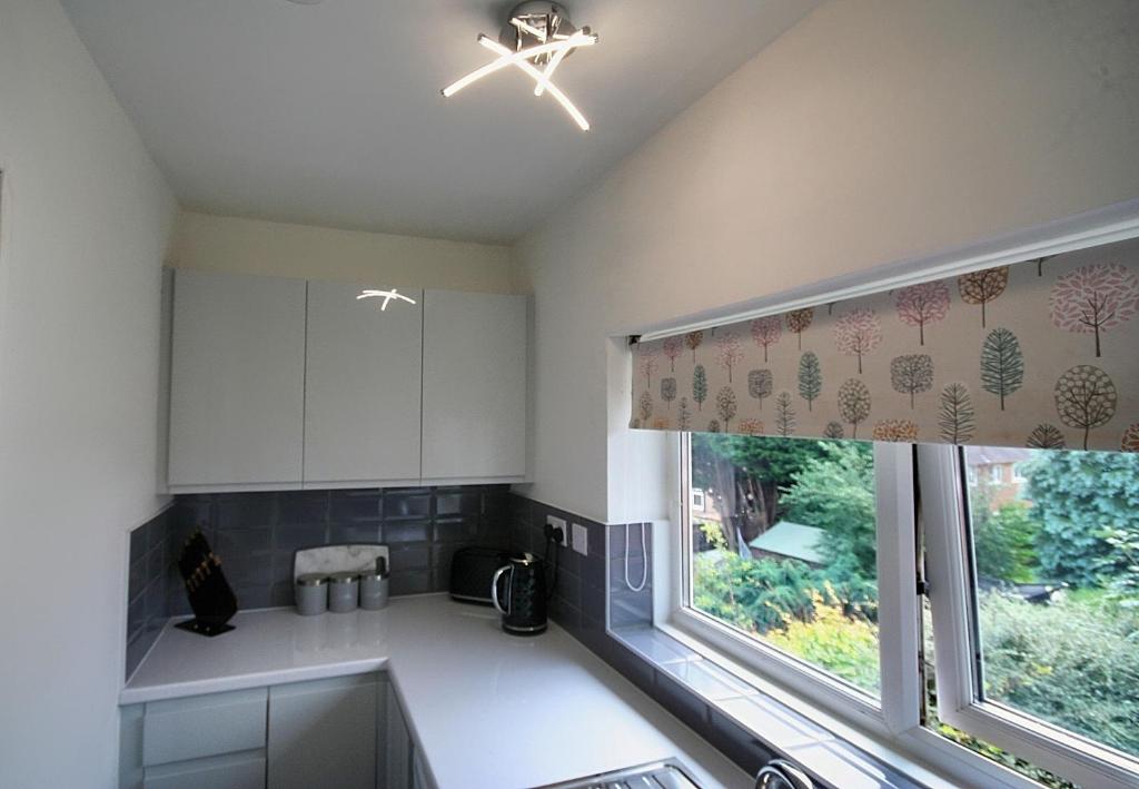 cocina con armarios blancos, ventana y fregadero en Sheffield serviced apartment, en Greenhill