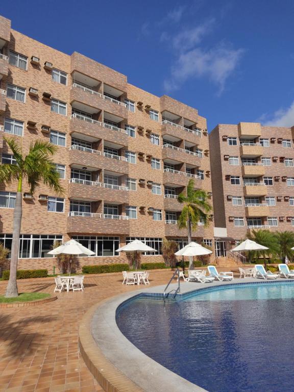 un grand bâtiment avec une piscine, des chaises et des parasols dans l'établissement Gran Lençóis Flat Barreirinhas, à Barreirinhas