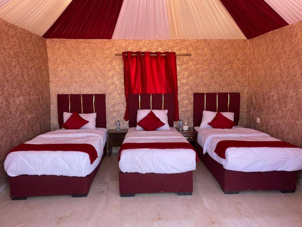 - 3 lits dans une chambre dotée de rideaux rouges dans l'établissement Beyond Wadi Rum Camp, à Wadi Rum