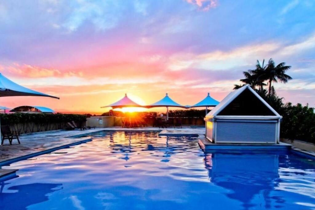 una piscina con una casa en el agua con una puesta de sol en The Entrance Serenity cove, en The Entrance
