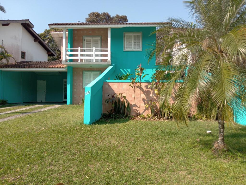 uma casa azul com uma palmeira em frente em Paraíso de Verão - Disfrute final de semana em Casa Exclusiva com piscina, sinuca e churrasqueira Aluguel para temporada em Riviera de São Lourenço em Bertioga