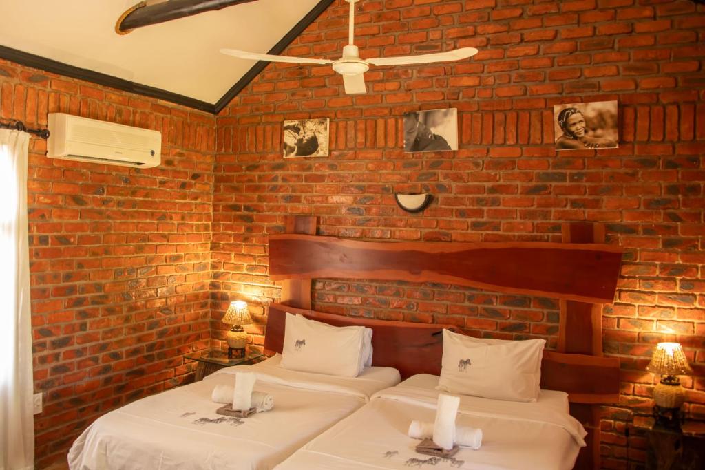 twee bedden in een kamer met een bakstenen muur bij Fiume Lodge CC in Grootfontein