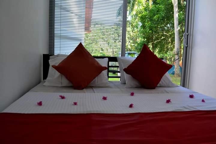 uma cama com almofadas vermelhas e brancas e uma janela em Diyagal Villa 