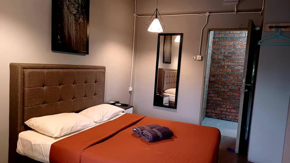a bedroom with a bed with an orange blanket and a mirror at BRICKS Cameron Hostel in Tanah Rata