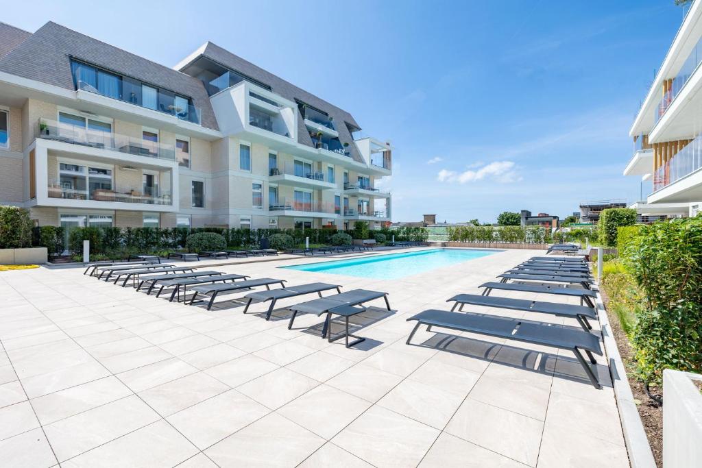 a swimming pool with lounge chairs in front of a building at VivaVela in Nieuwpoort