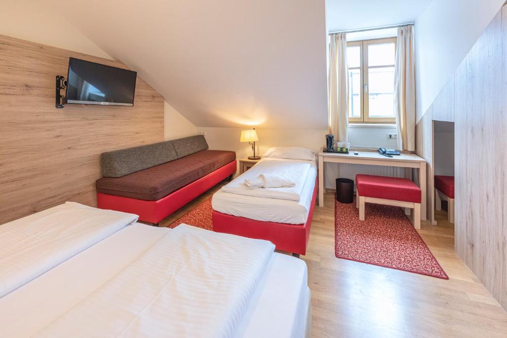 a room with two beds and a desk and a tv at Hotel Eder in Munich
