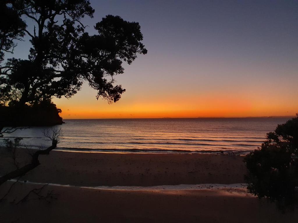 una puesta de sol sobre el océano con una playa en Whangaparaoa Lodge en Whangaparaoa