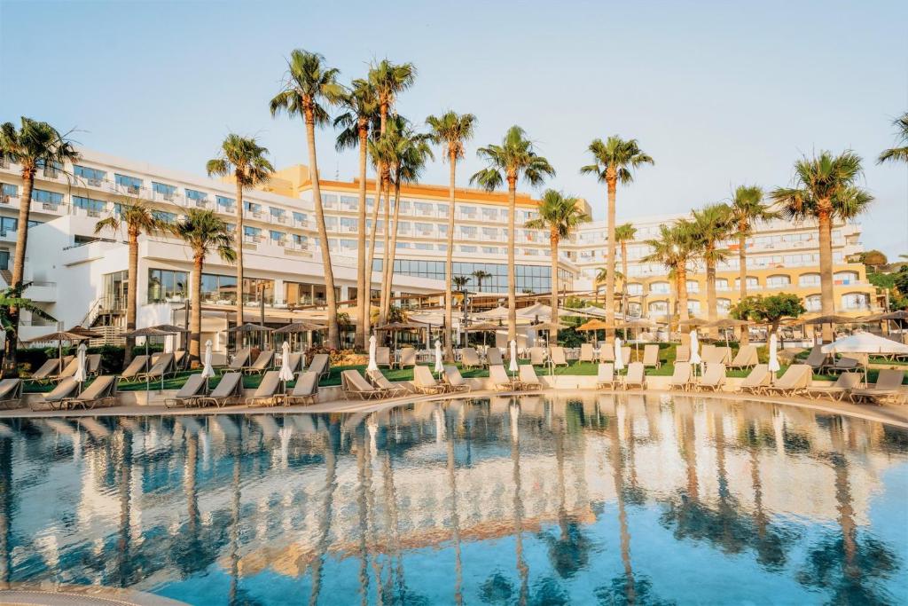 Il propose une grande piscine avec des chaises et des palmiers. dans l'établissement St George Beach Hotel & Spa Resort, à Paphos