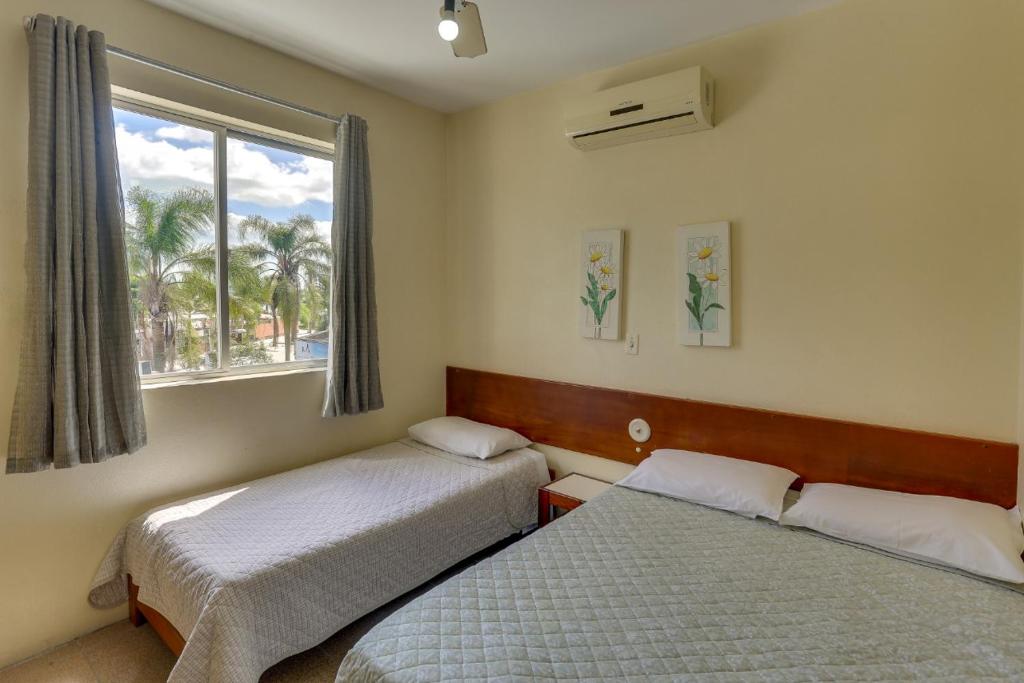 1 dormitorio con 2 camas y una ventana con palmeras en Canascenter Apart Hotel, en Florianópolis