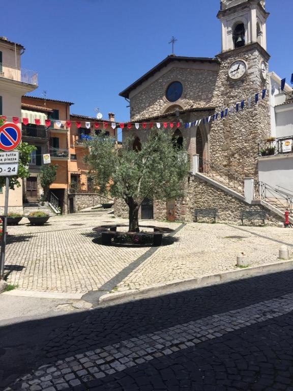 um edifício com uma torre de relógio e uma árvore num pátio em Short let SanRocco em Olevano Romano