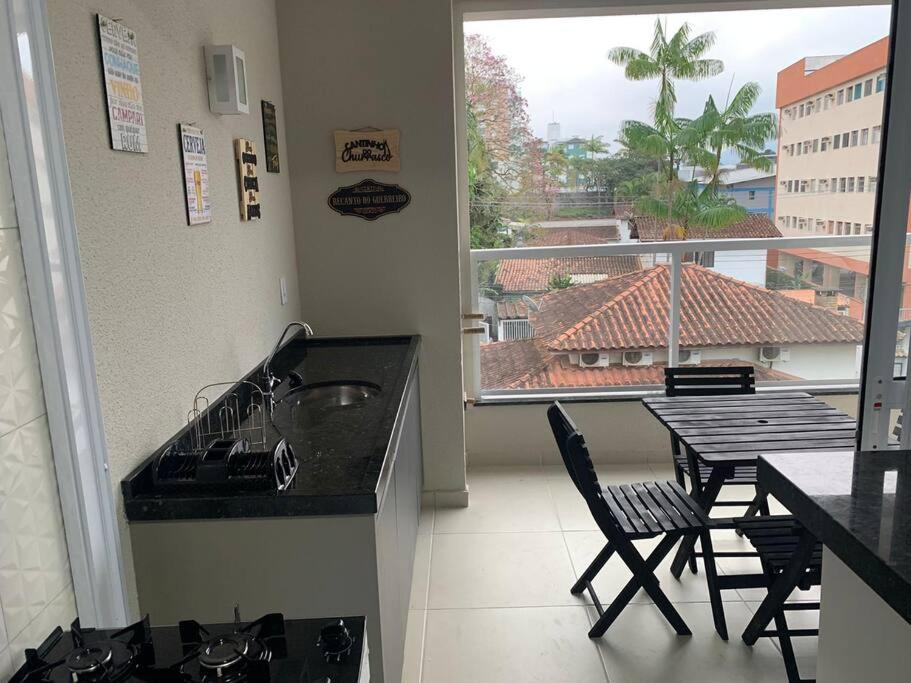 eine Küche mit einer Spüle und einem Tisch sowie einen Balkon in der Unterkunft Alto Padrão Tenório 2suites com ar, wifi e piscina in Ubatuba