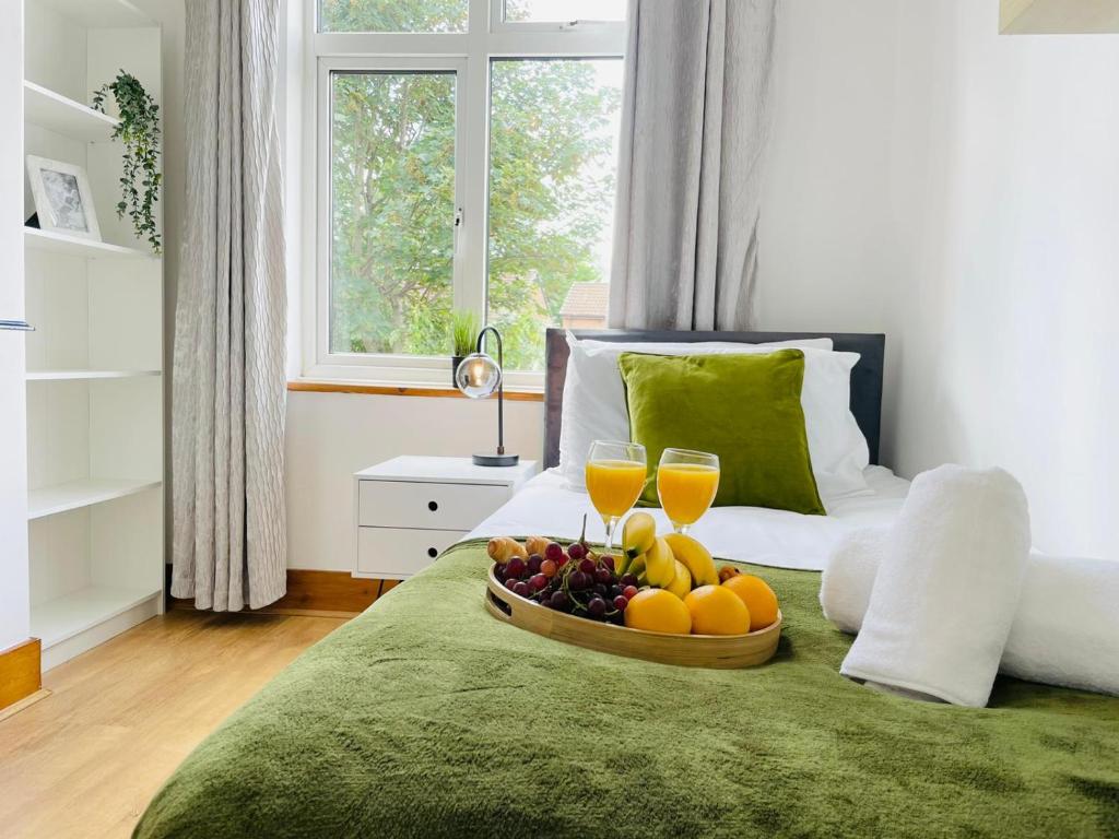 a tray of fruit on a bed with two glasses of orange juice at 4-Bed House Sleeps 7 with Garden in Luton