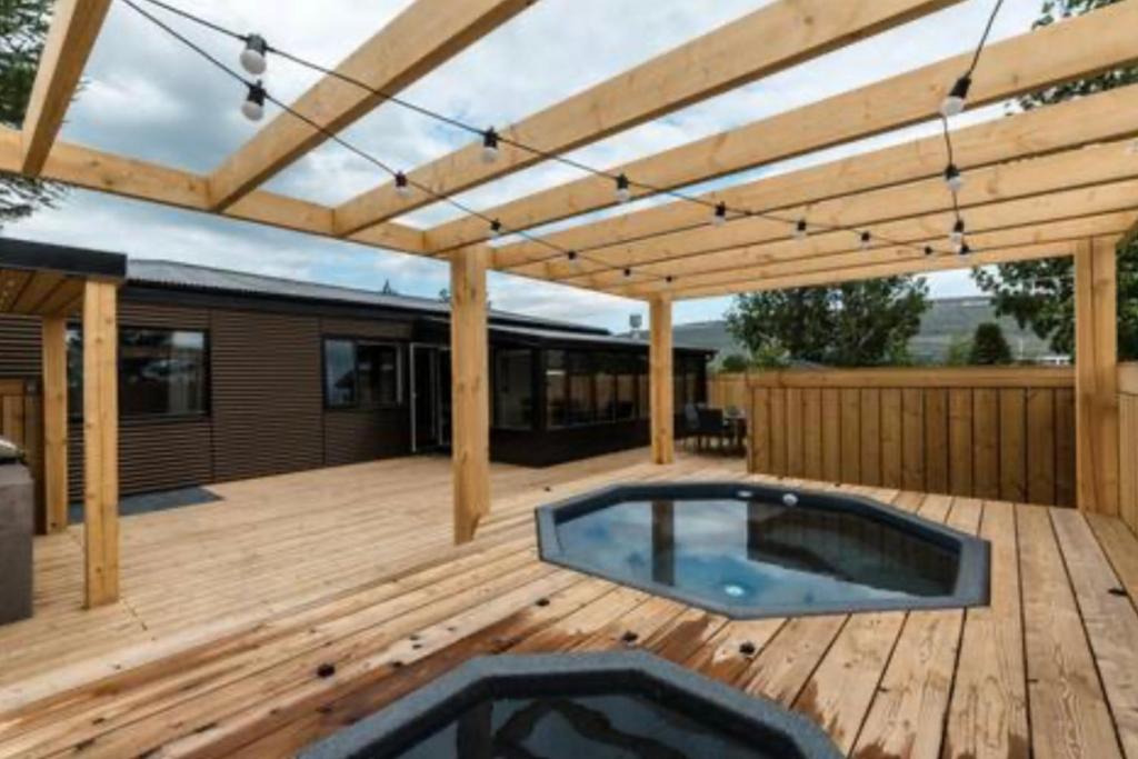 una terraza de madera con una piscina bajo una pérgola de madera en Private house in the center of Akureyri 