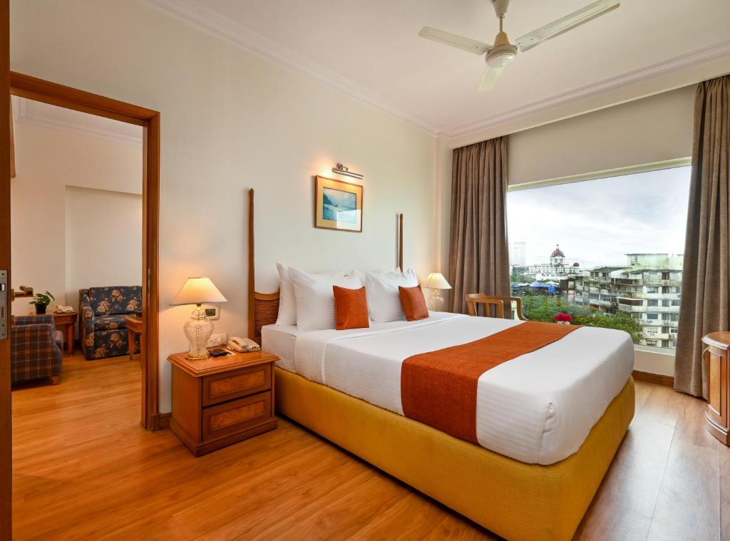 ムンバイにあるFariyas Hotel Mumbai , Colabaのベッドと大きな窓が備わるホテルルームです。