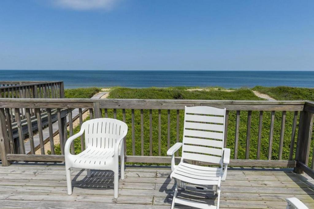 two white chairs sitting on a deck overlooking the ocean at The Ferdinando at Ships Watch in Duck