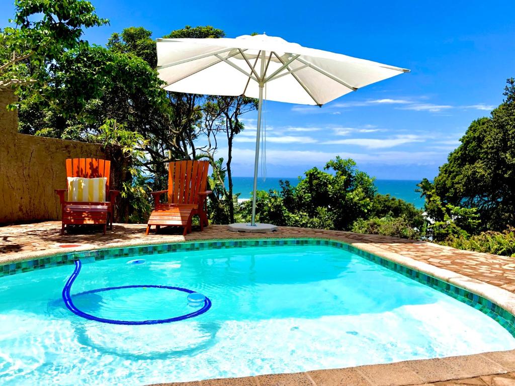 a swimming pool with an umbrella and chairs at COCOVIEW BEACH HOUSE in Southbroom