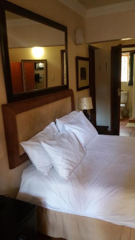 ein Bett mit weißer Bettwäsche und einem großen Spiegel in der Unterkunft Harties Lodge - Bay View 5 in Hartbeespoort