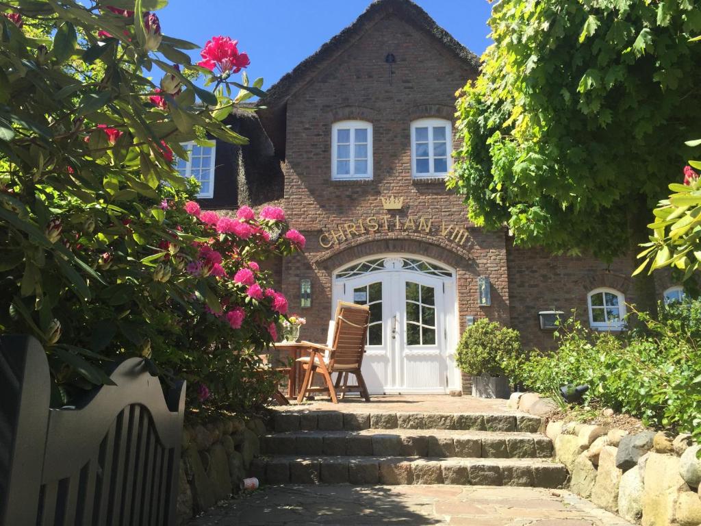 an old brick building with a porch and flowers at Hotel Parkresidenz Christian VIII in Archsum