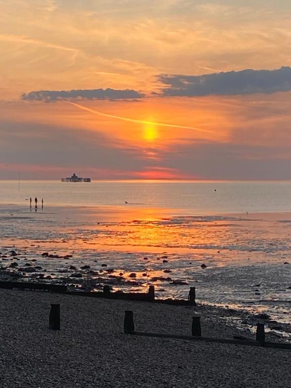 a sunset on the beach with people in the water at Stylish contemporary seaside holiday home with 5 bedrooms, sea view, parking and EV point in Kent