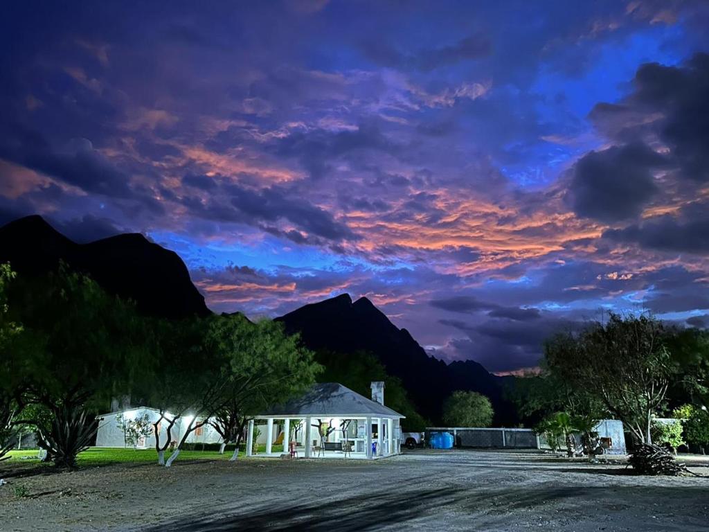a cloudy sky with a house and mountains in the background at Casa de campo la huasteca in Monterrey