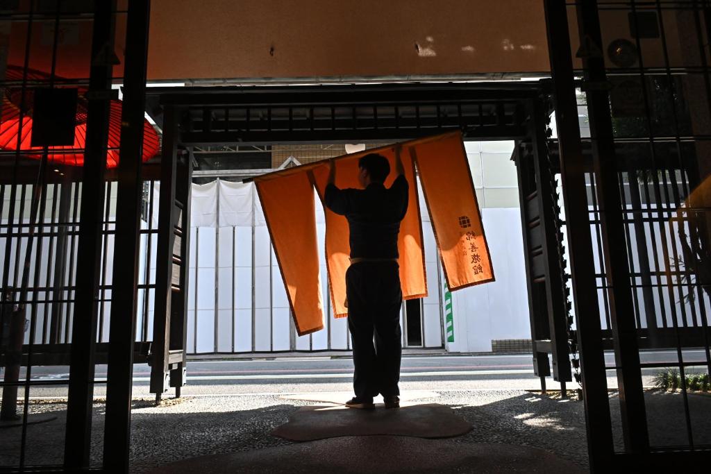 a man standing in a gate holding a flag at Watazen Ryokan - Established in 1830 in Kyoto
