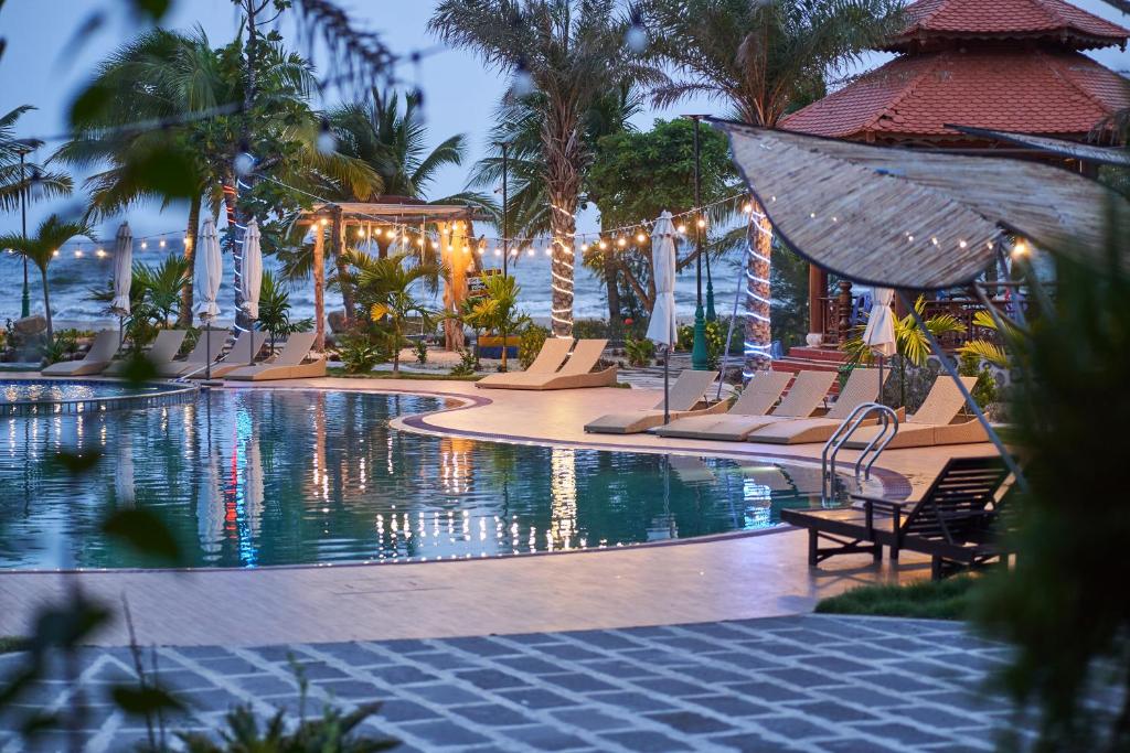 a pool at a resort with chairs and palm trees at Hodota Cam Bình Resort & Spa - Lagi Beach in Vĩnh Thạnh