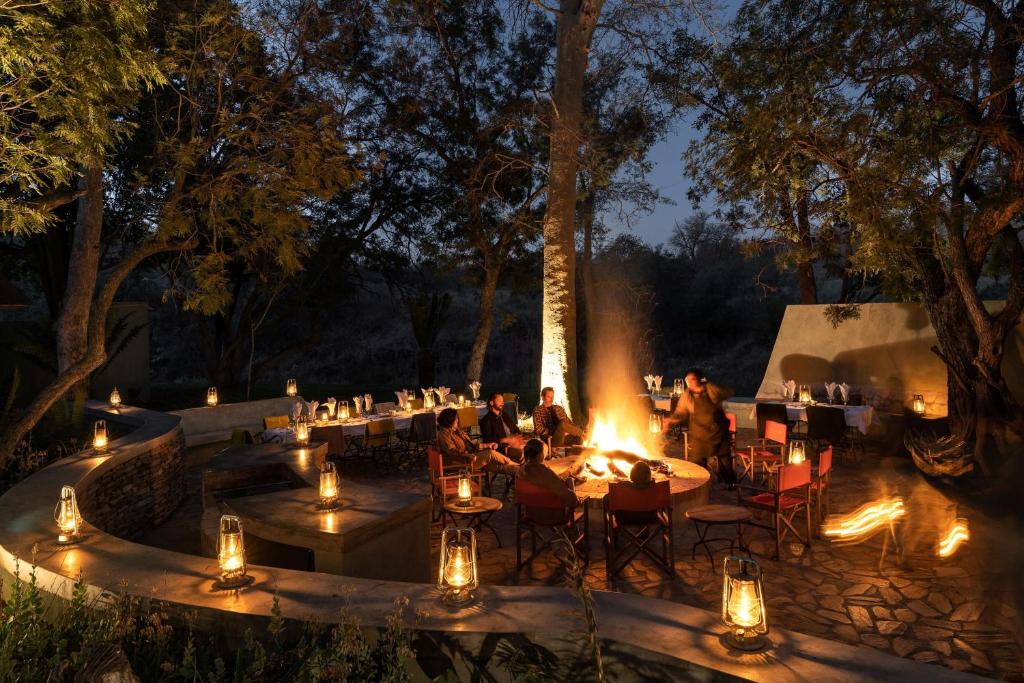 a group of people sitting at tables with fire at night at Simbavati Camp George in Klaserie Private Nature Reserve