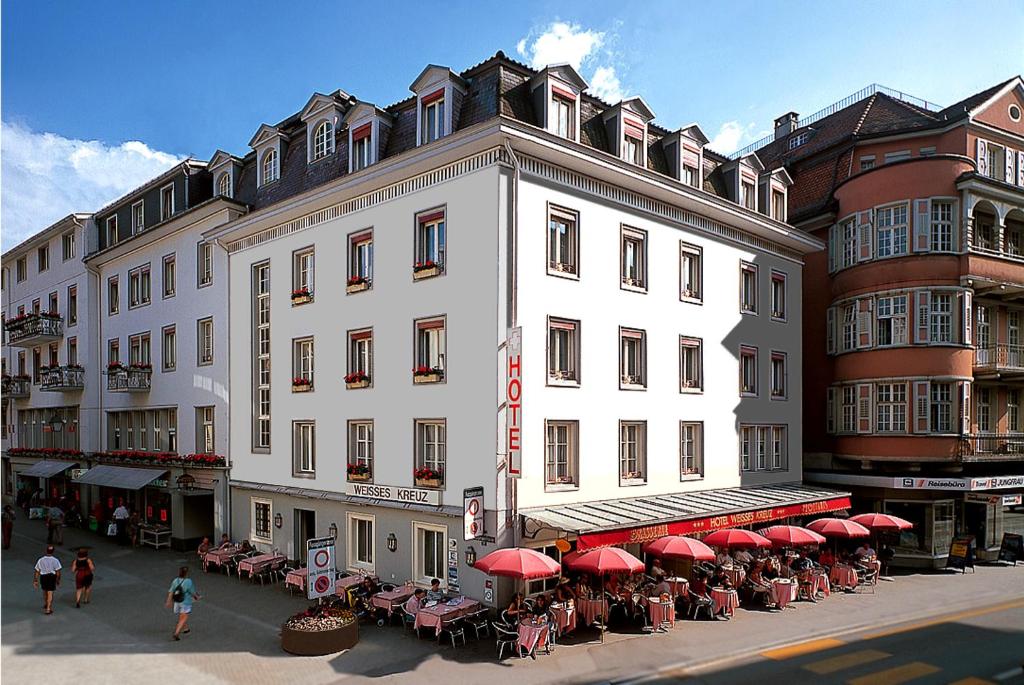 een groot wit gebouw met tafels en rode parasols bij Hotel Weisses Kreuz in Interlaken