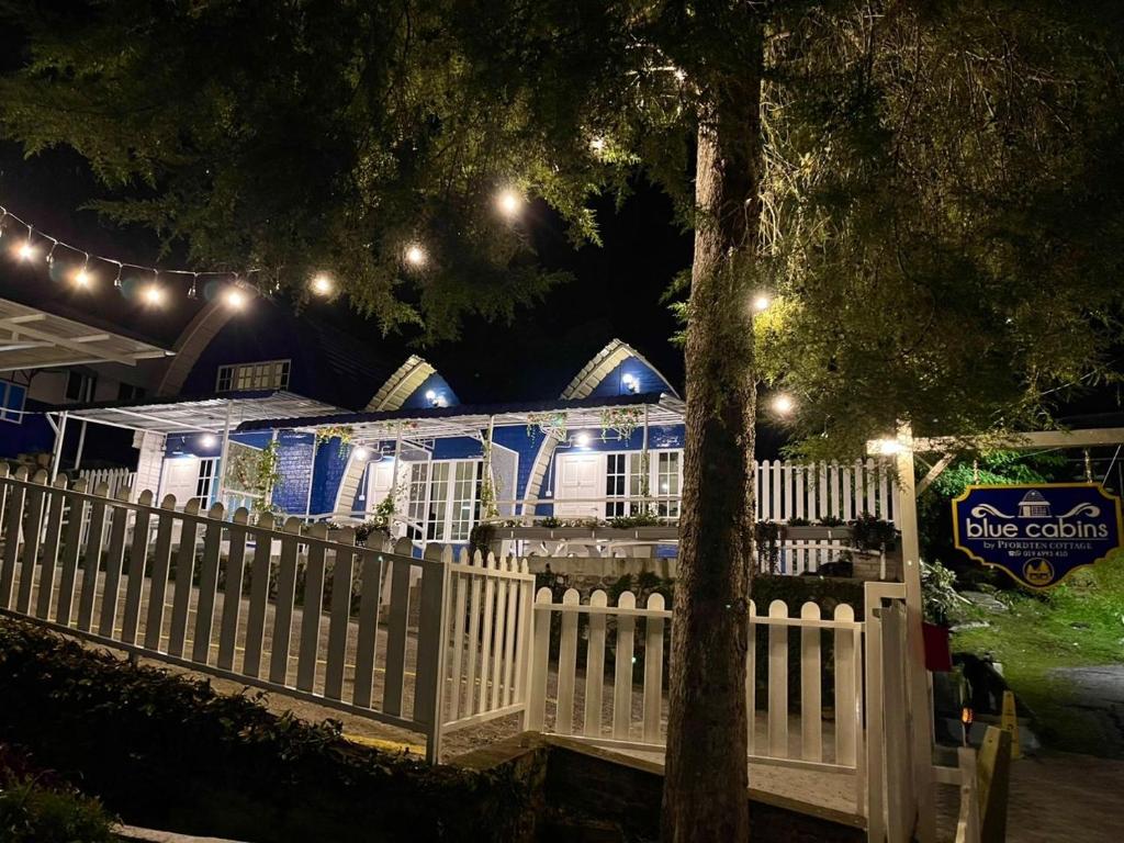 a white fence in front of a house with lights at Blue Cabins By Pfordten Cottage in Cameron Highlands