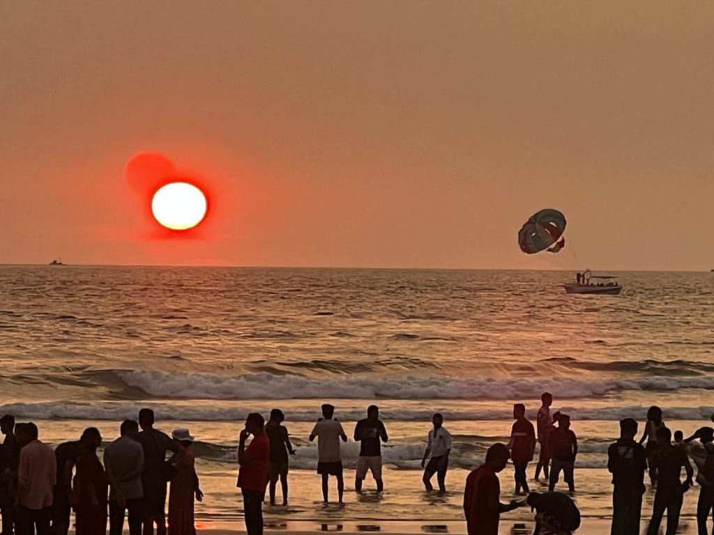 een groep mensen die op het strand staan te kijken naar de zonsondergang bij Baga Fantacia Beach Inn in Calangute