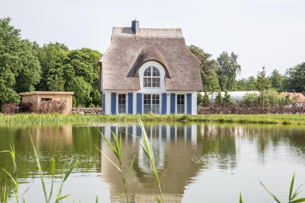 a house with a thatched roof reflected in a pond at Ferienhaus Schilfrohrsaenger 31 in Fuhlendorf